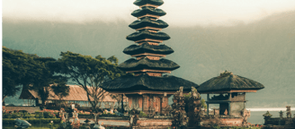 Traditional Thai temple with layered rooftops set against misty mountains and tropical trees at dawn