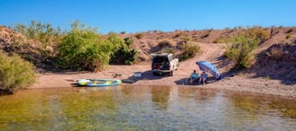 day camp setup on coloardo river with 4runner, 2 people, umbrella and paddle boards by the water