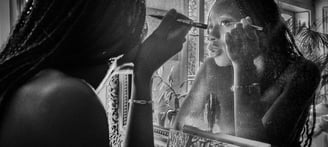 Photo artistique noire et blanc d'une jeune femme noire qui se requi se remaquille dans le miroir d'un intérieur haussmannien