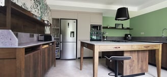 Cuisine en chêne teinté et colonnes beige. Plan de travail en pierre. Poignées cuir. Hotte suspendue