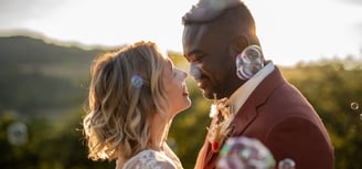 a bride and groom in front of blowing bubbles in the air, in front of the sunset