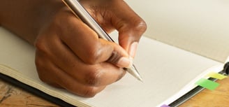 a person holding a pen and writing on a notebook