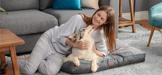 a woman sitting on a dog bed with her dog