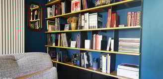 Bibliothèque sur mesure aménagée dans une niche bleue dans le salon TV. Étagères OSB, support tôle.