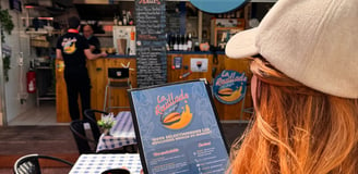 Une jeune femme lit le menu de La Rouillade lors d'une journée ensoleillée.