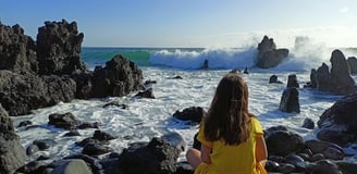 a little girl sitting on rocks before the ocean