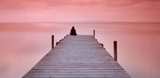 A person sitting alone at the end of a jetty on a calm evening. The scene depicts the Lonely Art of Art