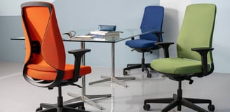 Three colorful Sensit T150 chairs in orange, blue, and green around a glass meeting table.