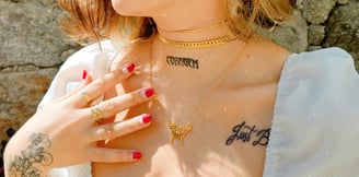 Foto do busto de mulher com roupa branca e joias em dourado.