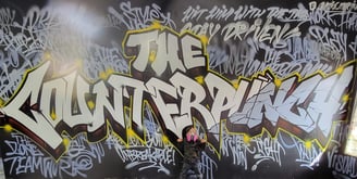 a kid standing in front of a graffiti - filled wall that reads "The Counterpunch"