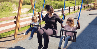 a mom sitting on a swing set with her two bilingual kids