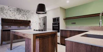 Cuisine en chêne massif avec plan en pierre. Armoire beige anti trace de doigts. Ilot Plaque mixte