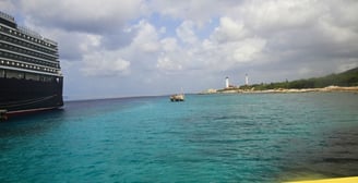 Vista do navio de cruzeiro ancorado na costa de Curaçao, com o mar azul e a cidade ao fundo.