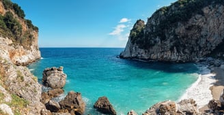 Vista da praia de Fakistra, em Vólos, na Grécia, com águas cristalinas e falésias ao redor.
