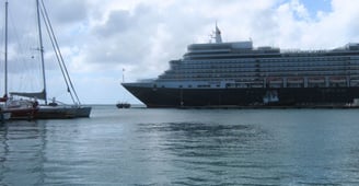 Navio de cruzeiro ancorado no porto de Oranjestad em um dia nublado, com a cidade ao fundo.