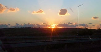Volta de carro ao entardecer, despedida de Nazaré com o pôr do sol iluminando a estrada.