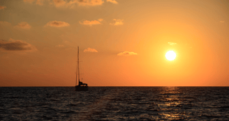 Horizonte durante el atardecer, con el cielo naranja, y el sol y un velero de fondo en el mar