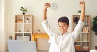 a very happy woman sitting at a desk with her arms up in the air