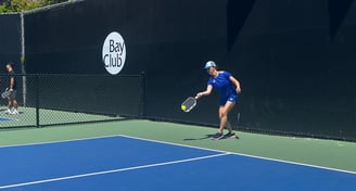 Pickleball player in blue outfit reaching for a low shot during pickleball training match.