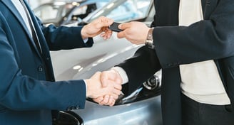 Remise de clés avec poignée de main entre deux personnes devant une voiture.