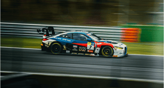 Auto GT in pista durante una gara ad alta velocità, con livrea sportiva e sponsor visibili