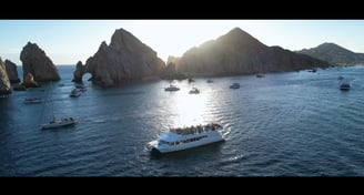 A drone's aerial perspective captures a boat gathering near the iconic Cabo San Lucas arch. Highlighting videography service