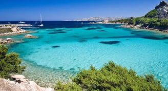 Aerial view of Costa Smeralda’s turquoise waters with luxury yachts anchored near a pristine beach.