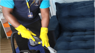 Homem de camisa azul e luvas amarelas limpando um sofá