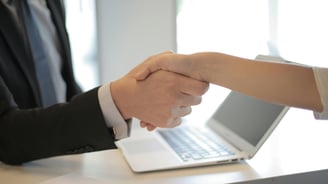 a man and woman shaking hands over a laptop