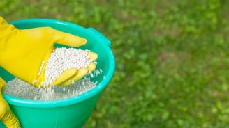 a person with a yellow glove sifting through fertilizer pellets in a yellow bucket