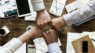 two people shaking hands over a desk with a laptop