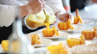 a person pouring a sauce on a plate with small pumpkins
