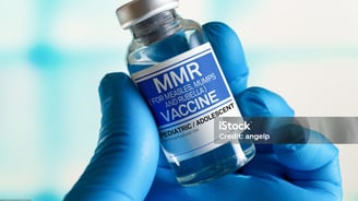 a person in blue gloves holding a vial of vaccine