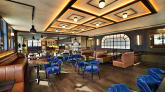 Modern restaurant interior with blue chairs and geometric lighting.