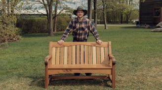 a man in a hat and plaid shirt standing in front of a bench