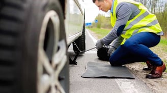 a man in a yellow vest is fixing a tire on a car