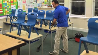 a man cleaning a classroom classroom with a vacuum