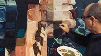 Martin Osner painting a textured mixed media artwork in his studio. He holds a palette of earthy paints an abstract portrait