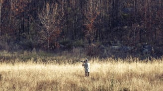 Martin Osner photographing in a golden field against a backdrop of burnt trees and mountain shadows.