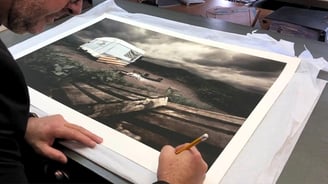 Martin Osner signing a limited edition Abandoned Collection fine art print, featuring a moody landscape with a old caravan