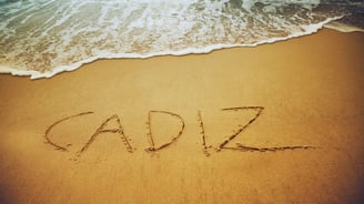 Foto de "Cádiz" escrito na areia da praia, com as ondas do mar ao fundo.