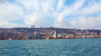 Navio chegando ao porto de Haifa visto do convés, com a cidade se estendendo ao pé do Monte Carmelo.