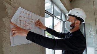 Engenheiro mostrando planta na parede de uma obra em andamento