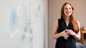 a woman in a black top and jeans standing in front of a white board