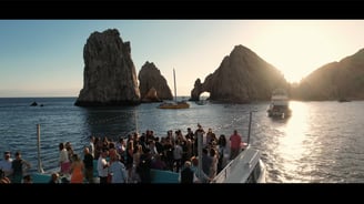 Captured moment of a pre-wedding gathering on a boat with the Cabo San Lucas arch visible in the background. Filmed for Weddi