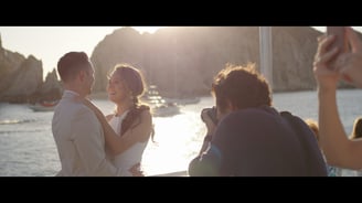 Photographer capturing images of a couple with the sea and yachts in the background, bathed in golden light; scene taken from
