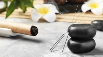 Acupuncture needles tilted on a table and Ayurvedic stones
