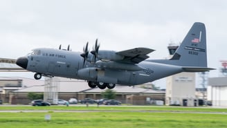 US Air Force Hurricane Hunter plane taking off with ground just below plane and control tower in back ground.