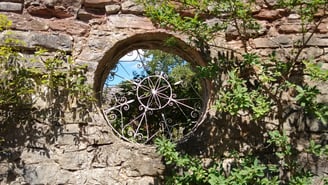 Picture of a stone wall with round opening and wrought iron design inside