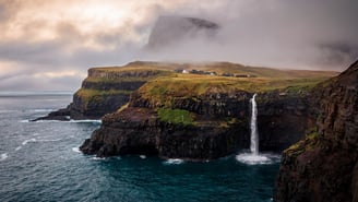 a waterfall falls down a cliff into a body of water, múlafossur Faroe Islands